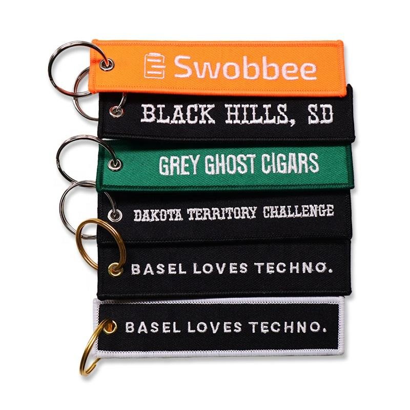 "Custom embroidered keychains featuring text like 'Black Hills SD', 'Grey Ghost Cigars', and 'Basel Loves Techno'."