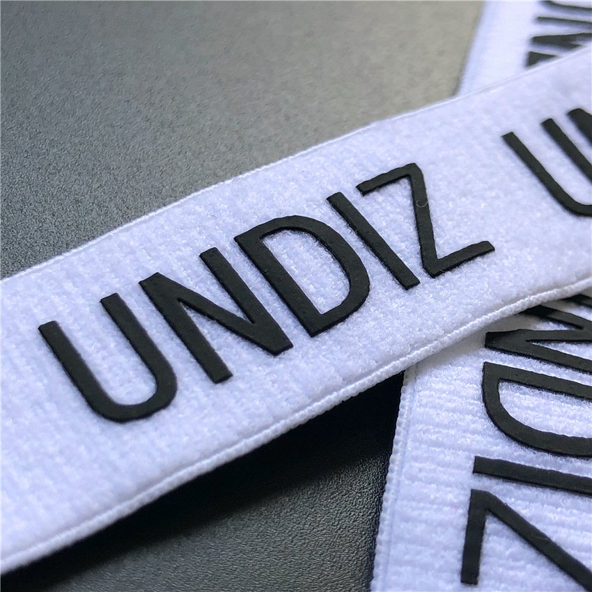 "White elastic webbing with bold black 'UNDIZ' lettering using heat transfer printing for branding and apparel customization."